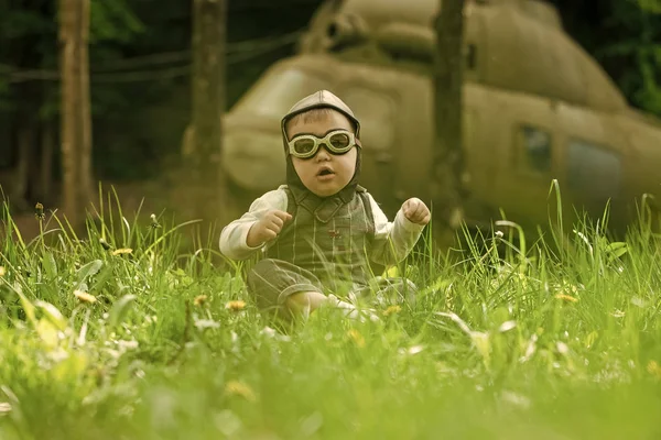 Chlapec v pilotní přilba a brýle sedí v zelené trávě — Stock fotografie