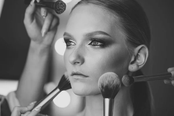 Mujer joven tiene pinceles alrededor de maquillaje de la cara — Foto de Stock