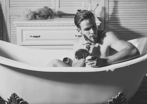 Grooming man shave with razor look at mirror in bathtub — Stock Photo, Image