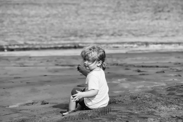 Söt baby boy sitter på sand på sandstrand — Stockfoto