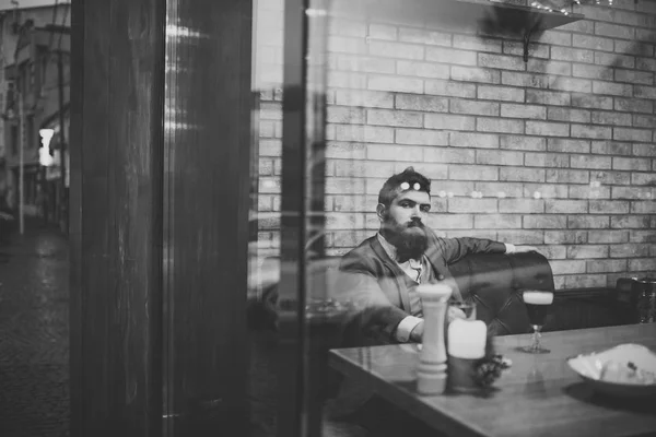 Bearded man rest in restaurant with beer glass. Beer time. serious bar customer sit in cafe drinking ale. Date meeting of hipster awaiting in pub. Businessman with long beard drink in cigar club.