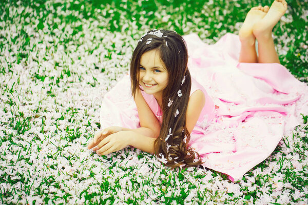 Little girl on green grass with petals