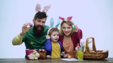 Paskalya yumurtaları ile mutlu bir aile. Mutlu bir aile Paskalya için hazırlanıyor. Baba, anne ve oğulları beyaz arka plan üzerinde izole Paskalya için hazırlanıyor yabani tavşan kulakları giyinmiş.