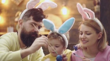Mutlu aile Paskalya için hazırlıyoruz. Sevimli küçük çocuk Bunny kulaklar giyiyor. Mutlu Paskalya kavramı. Sakallı adam sarışın bir kadın ve bir tavşan kulakları giymiş küçük bir çocuk yumurta boyama