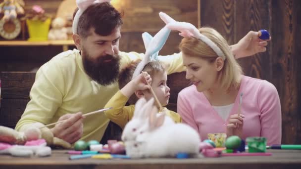 Mor, far og søn maler æg. Lykkelig familie forbereder sig til påske. Sød lille dreng iført kaninører. Glædelig påske . – Stock-video