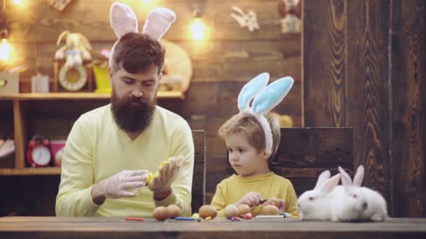 Padre e hijo están pintando huevos. La familia feliz se está preparando para la Pascua. Lindo niño con orejas de conejito. Feliz Pascua. . — Vídeo de stock