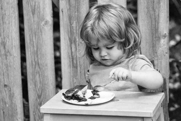 Small boy eating pie near wooden fence — Stock Photo, Image