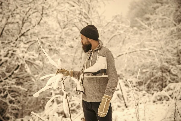 Bebaarde man houd schaatsen in de winter van de besneeuwde bos, Kerstmis — Stockfoto