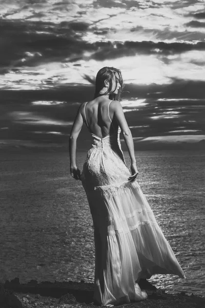 Söt flicka i vit klänning står på dark sea shore — Stockfoto