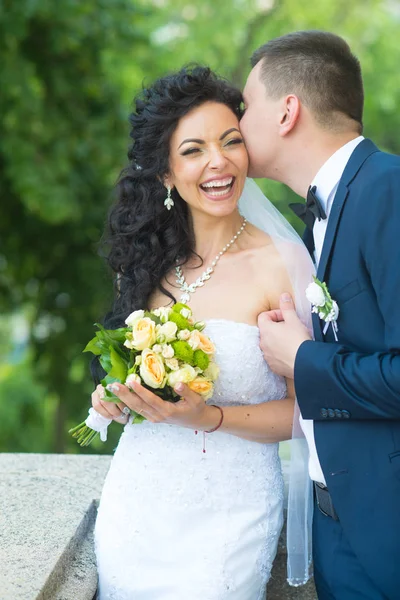 Bruidegom kus gelukkige bruid met boeket. Vrouw en man glimlach op de trouwdag. Bruidspaar in liefde. Jonggehuwde paar op zomer buiten. Huwelijk concept. liefde en familie — Stockfoto