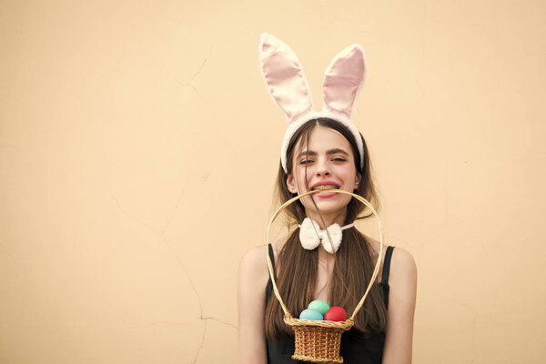 Easter girl holding wicker basket with eggs in teeth