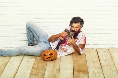 Cadılar Bayramı zombi adam, uzun sakalı sakallı, acımasız beyaz hipster kırmızı kanlı gömlek ciddi yüzüne bıyık ile kabak, yaralar ve beyaz tuğla duvar arka plan üzerinde kırmızı kanlı balta tutar