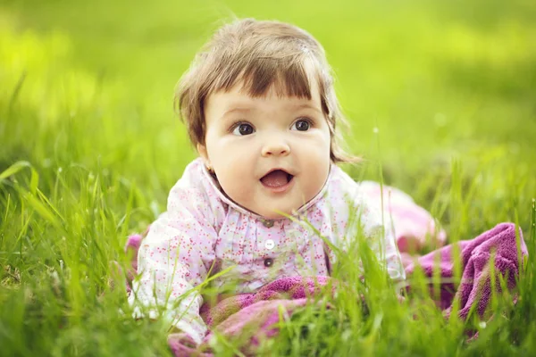 きれいな顔と自然な背景の屋外の緑の草の上に座って面白い目の小さなかわいい女の子 — ストック写真