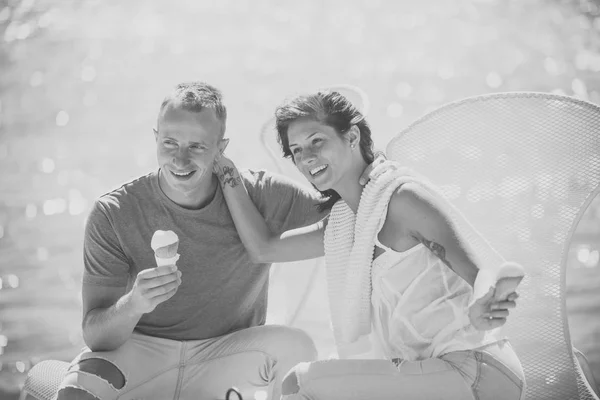 Casal apaixonado por sorvete nas mãos, superfície do mar cintilante no fundo, desfocado. Casal bonito gosta de férias de verão. Casal come sorvete na praia, sorvete e conceito de verão . — Fotografia de Stock