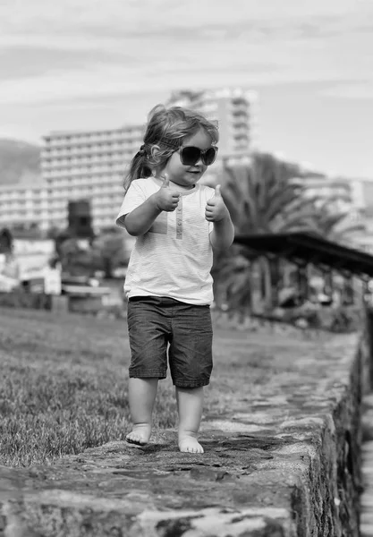 Lindo bebé feliz niño en gafas de sol muestra los pulgares hacia arriba gesto — Foto de Stock