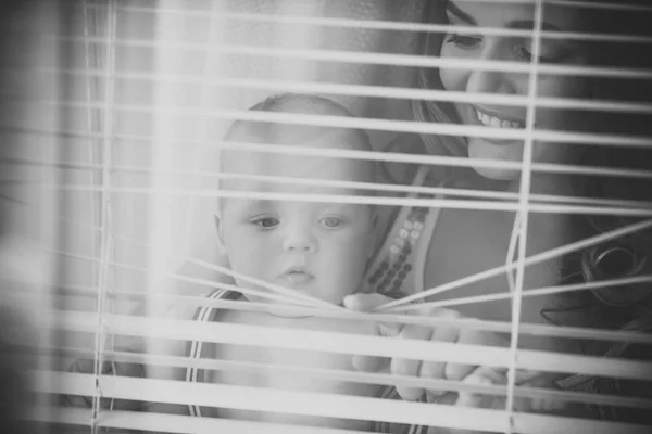 Baby son and mother open blinds — Stock Photo, Image