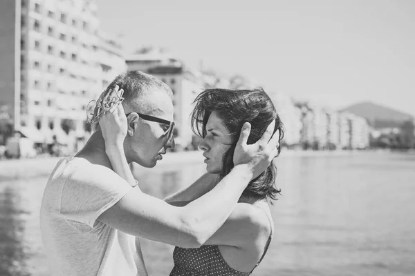 Familia feliz pasar tiempo juntos, abrazos, mar y fondo urbano. Pareja enamorada parada en primera línea de mar. Concepto de vacaciones familiares. El hombre sostiene a las mujeres cabeza, pareja en caras pensativas. Concepto de amor . —  Fotos de Stock