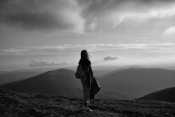 Pretty girl hiker in summer dress travel with backpack on mountain peak over cloudy sky