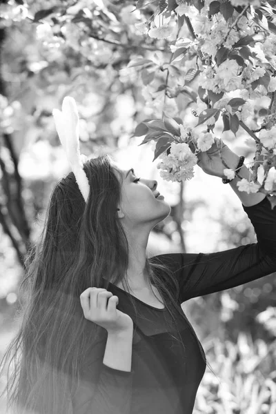 Menina com orelhas rosadas coelho cheirando flores sakura da árvore — Fotografia de Stock