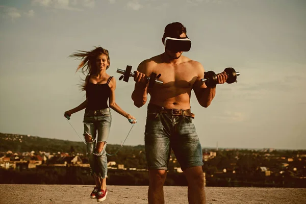 Atletas no ar fresco. Atletas treinando juntos. Homem atleta usar óculos VR com halteres, enquanto a mulher pulando com corda. Atletas fortes ao ar livre. Força do seu lado — Fotografia de Stock