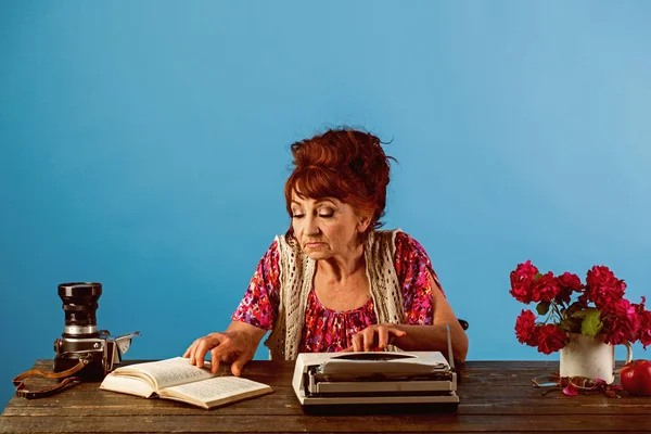 Geschoolde arbeider. Oude vrouw werk in schrijver kantoor. Senior schrijver aan balie. Vrouwelijke verslaggever of journalist schrijven op typemachine. Journalist werken in vintage kantoor. Senior vrouw type op retro typemachine — Stockfoto