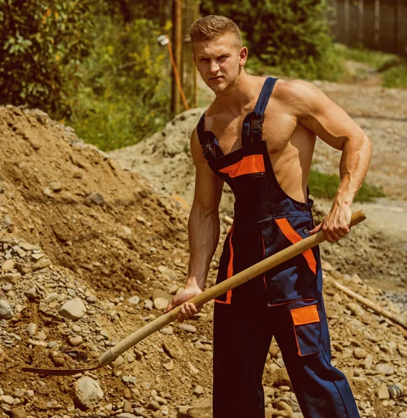 Pojetí člověka. Muž s lopatou v pracovních uniformách. Muži pozemní dig. Silný muž s lopatou v svalnaté ruce — Stock fotografie
