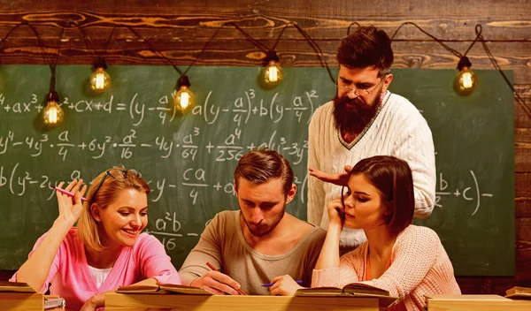 Students, group mates speaking, asking for advice, teacher explains. Studying difficulties concept. Bearded teacher, lecturer, professor teaching students, chalkboard on background — Stock Photo, Image