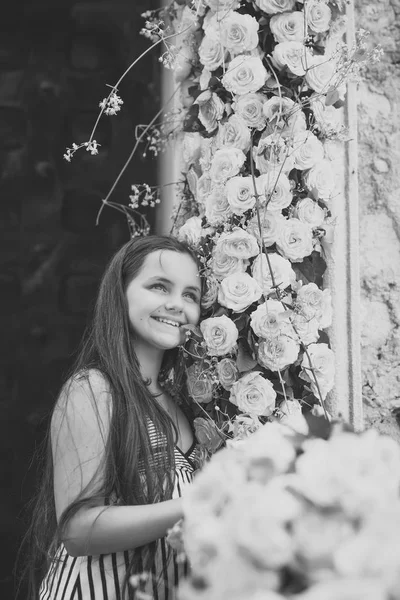 Nettes kleines Mädchen lächelt mit einer Menge gelber Rosen — Stockfoto