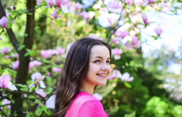 Vrolijke lente dag. Schattig meisje glimlach in park met bloeiende bloemen. Mooi meisje in de buurt van bloeiende boom geniet van magnolia bloesem. Schattig meisje gelukkig lachend op lente landschap. De lentetijd — Stockfoto