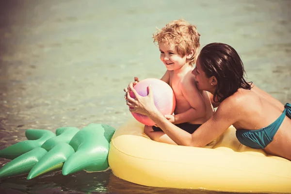 Sommerurlaub und Reise ans Meer. glückliche Familie am karibischen Meer. Malediven oder Mami Strand Aktivität Freude. Mutter und Sohn spielen am Muttertag Ball im Wasser. Ananas aufblasbare Matratze, Jahrgang. — Stockfoto