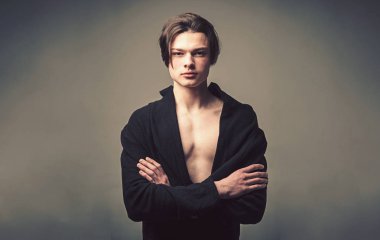 Adam siyah bornoz emin yüzündeki katlanmış, gri arka plan silah tutar. Maço şık uzun saç kesimi ile. Erkeklik kavramı. Pürüzsüz cilt üzerinde yüz, boyun ve göğüs kameraya bakarak adam.