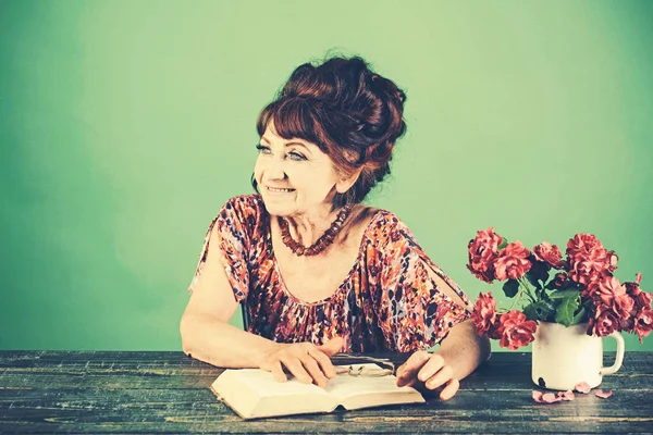 Old woman reading book with glasses at flowers.