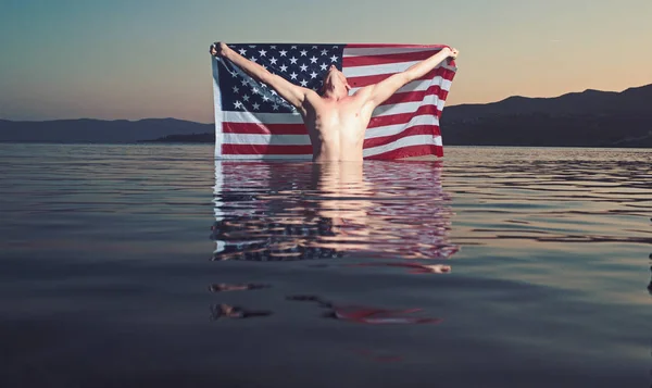 Amerikanische Flagge im Wasser mit sexy Mann. Unabhängigkeitstag. Sommerurlaub und paradiesischer Urlaub. Mann mit sexy Körper entspannen am Strand. Nackter Macho im Meerwasser — Stockfoto