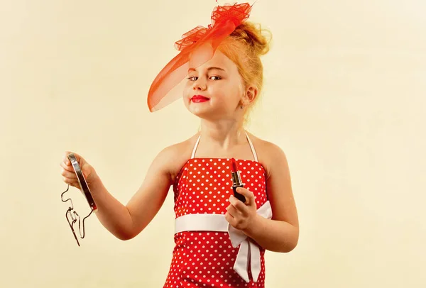 Look rétro maquillage et coiffeur. Enfant fille en robe élégante, maquillage. Mode fille rétro avec cosmétiques, beauté. Mode et beauté, style pin-up, enfance. Petite fille tenir rouge à lèvres et miroir . — Photo