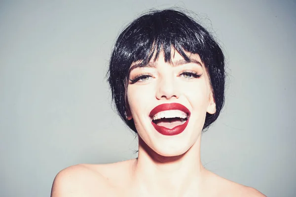 Chica en la cara sonriente feliz posando con hombros desnudos. Señora de peluca negra con maquillaje sobre fondo gris. Hermoso concepto de sonrisa. Mujer con atractivos labios rojos mira a la cámara . — Foto de Stock