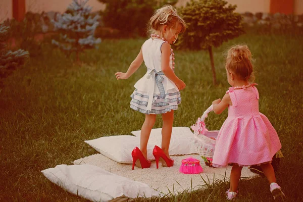 Сёстры в стильных платьях играют на зелёном газоне — стоковое фото
