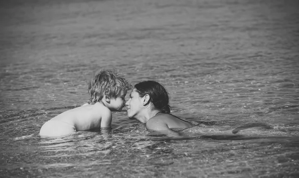 Mom and kid with smiling faces spend time together in sea on sunny day. Cute child boy play with mom in sea water, touch her nose. Motherhood concept. Mother swimming in sea and look at child. — Stock Photo, Image