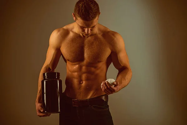 Healthy diet. Vitamin nutrition. Strong man hold vitamin bottles. Man with six pack ab. Stimulating muscle growth with anabolic steroids. Anabolic hormone increases muscle strength. High protein diet