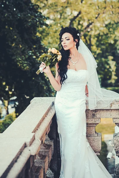 バルコニーで花を持つ女性。結婚式のブーケとの官能的な女性。ブライダルメイクやヘアスタイルと美しさの少女。白いファッションのドレスとベールの花嫁。結婚式のファッションと流行 — ストック写真