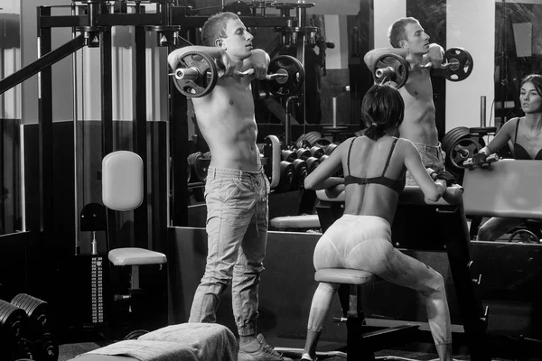 Musculoso homem e menina no ginásio com halteres e barra — Fotografia de Stock