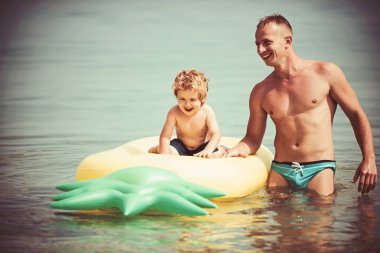 Maldivler veya Miami beach etkinlik sevinç. Baba ve oğul babalar gününde yüzmek. Ananas şişme veya hava yatağı. Karayip Denizi üzerinde mutlu bir aile. Yaz tatil ve seyahat okyanus, vintage.