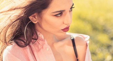 Kadın sakin yüz makyaj ile arka plan, doğa defocused. Büyük yüzük küpe kızla açılarak gömlek ve siyah iç çamaşırı giyer. Bayan çıplak omuz ile çekici görünüyor. Kadınlık kavramı