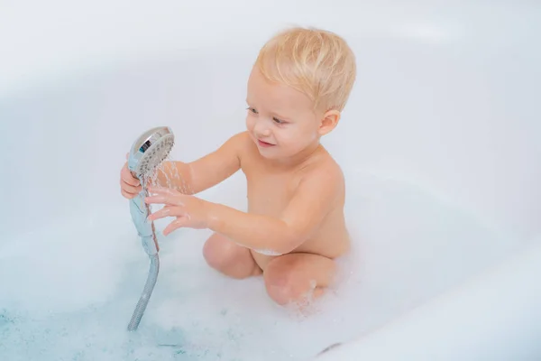 Lustiges Baby, das in einer großen Küchenspüle mit Wasser und Schaum spielt. schöner kleiner Junge mit Schaumbad. — Stockfoto