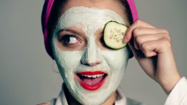 Žena nosí ručník a obličejové masky. Koncept péče o tvář. Atraktivní mladá žena, její oči okurky na šedém pozadí. Žena s hydratační maska. — Stock video