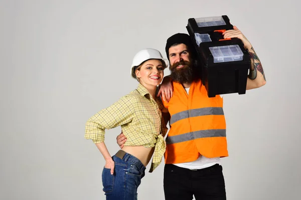 Accuracy of fixing. Pretty woman and bearded man in workwear. Builders or building technicians hold repair kit. Couple of construction workers. Renovation and construction. Couple of hard workers