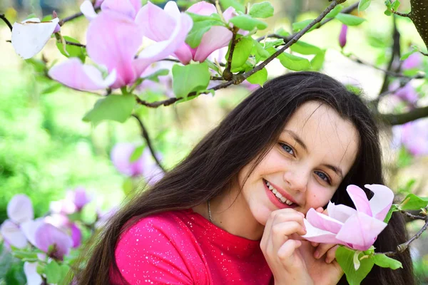 Ідеальний весняний день. Красива дівчина біля квітучого дерева насолоджується цвітінням магнолії. Чарівна дівчина посміхається в парку з квітучими квітами. Мила дівчина щаслива посміхається на весняному пейзажі. Весняний час — стокове фото