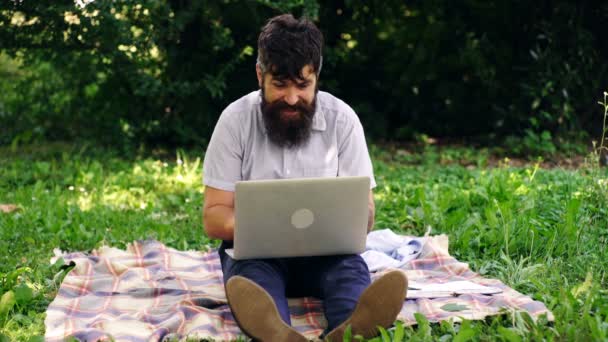 Un hombre feliz con una computadora al aire libre. Guapo hipster usando portátil en el parque en un día de verano. Concepto de oficina móvil . — Vídeos de Stock