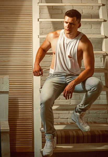 Guy în top rezervor la modă și blugi moda. Tânărul stă pe scară. Mașină atletică cu piept muscular și mâini. Modelul de moda cu par elegant. Mens stil de moda si trend — Fotografie, imagine de stoc