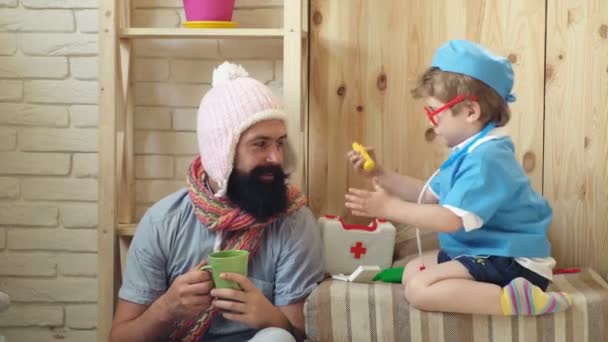 Padre e hijo jugando. Padre e hijo sonríen mientras pasan tiempo juntos. Un chico vestido de doctor jugando con papá. Padre e hijo jugando al hospital en casa. Concepto de medicina . — Vídeos de Stock