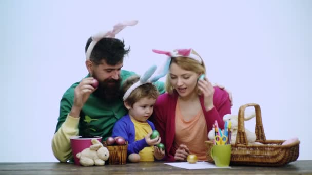 어머니, 아버지, 아들은 달걀에 그림을 그리고 있습니다. 행복 한 가족이 부활절을 준비하고 있다. 토끼 귀를 두르고 있는 귀여운 꼬마 소년. — 비디오